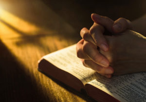 Close up of hands clasped on open Bible